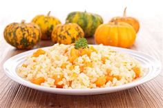 rice and pumpkins on a table with a white plate in the foreground, two gourds to the side