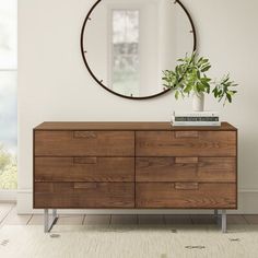 a modern dresser with a round mirror on the wall above it and a potted plant