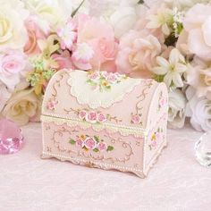 a small pink box sitting on top of a table next to flowers and glassware