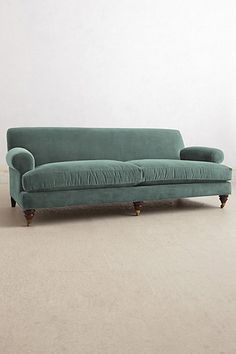 a green couch sitting on top of a hard wood floor next to a white wall