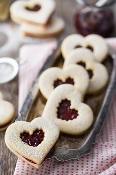 heart shaped cookies with jam in the middle on a tray next to silver spoons