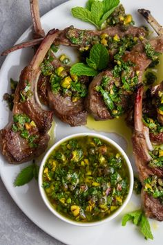 a white plate topped with steaks covered in green sauce and garnished with herbs