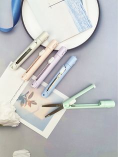 four different colored pens sitting on top of a white plate next to a blue ribbon