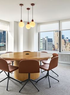 a round wooden table surrounded by four chairs in an office with large windows overlooking the city