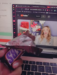 a person is holding a chocolate bar in front of a laptop computer with an image of a woman on the screen