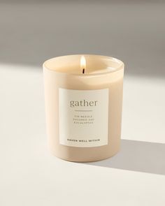 a candle that is sitting on a table next to a white wall with the words gather written in it