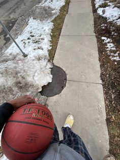 a person sitting on the sidewalk with a basketball in front of them and snow all over the ground