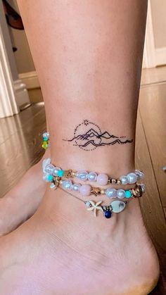 a woman's foot with a tattoo on the ankle and some beads around her ankles