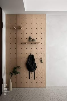 a wooden wall with hooks and a coat hanging on it's side, next to a potted plant