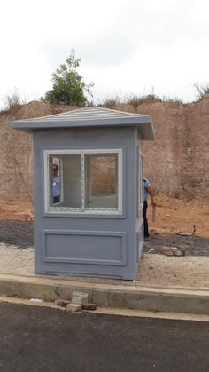 a small gray building sitting on the side of a road next to a dirt field