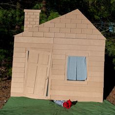 a cardboard house with a doll laying on the ground next to it