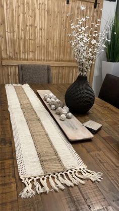 a wooden table topped with a black vase filled with flowers and white tassels