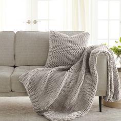 a couch with a blanket on top of it next to a potted plant and window