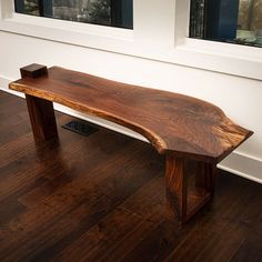 a large wooden bench sitting on top of a hard wood floor next to two windows