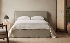 a bed with white linens and pillows in a neutral colored room next to a chair