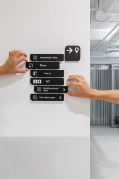 two hands pushing buttons on a white wall in an office building, with other hand pointing at them