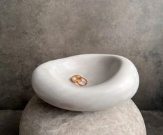 two gold wedding rings sitting on top of a white stone bowl that is shaped like an oval