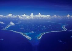 an island in the middle of the ocean surrounded by clouds and blue water is seen from above