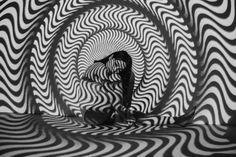 a black and white photo of a woman standing in front of a large, wavy tunnel