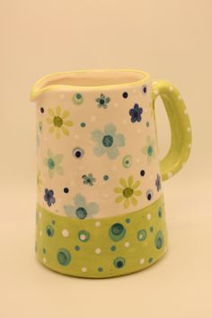 a green and white flowered pitcher with polka dots on the bottom, sitting in front of a beige background