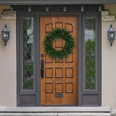 a front door with a wreath on it and two lights hanging from the side wall