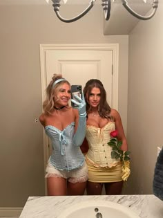 two women in corsets taking a selfie in front of a bathroom mirror