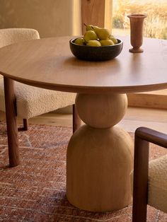 a bowl of fruit sitting on top of a wooden table next to two white chairs