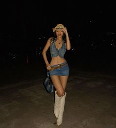 a woman in short skirt and cowboy hat walking on the street at night with her purse