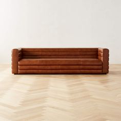 a brown leather couch sitting on top of a hard wood floor next to a white wall