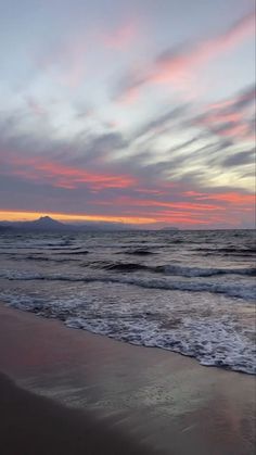 the sky is pink and blue as it sets over the ocean with waves coming in