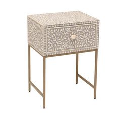 a white and gold side table with an intricate design on the top, sitting against a white background