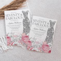 two wedding cards with floral designs on them sitting next to a tasseled piece of fabric