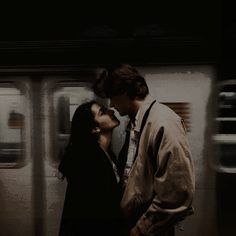 a man and woman standing next to each other in front of a subway train at night