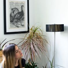 a woman sitting in front of a potted plant next to a wall mounted print