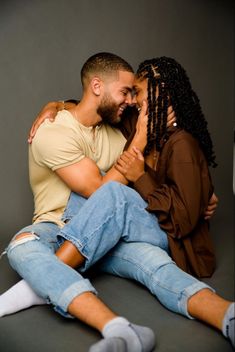 a man and woman sitting on the floor hugging each other with their arms around one another