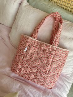 a pink floral bag sitting on top of a bed next to pillows and pillow cases