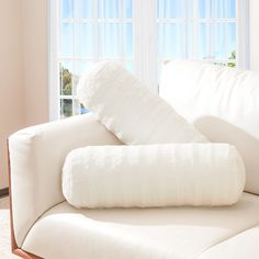 a white couch with two pillows on it in front of a window and some windows