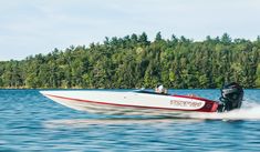 a speed boat speeds across the water with trees in the background