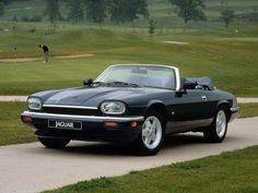 a black sports car parked on the side of a road next to a golf course