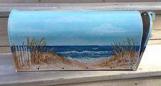 a painted mailbox sitting on top of a wooden bench next to the ocean and beach