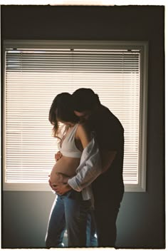 a man and woman standing next to each other in front of a window with blinds