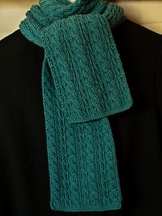 a green knitted scarf hanging on a coat hanger in front of a black shirt