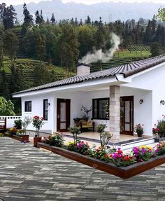 a white house with flowers in the front yard and mountains in the backgroud