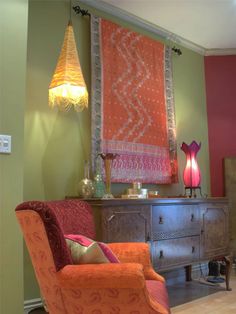 an orange chair sitting in front of a dresser with a lamp on top of it