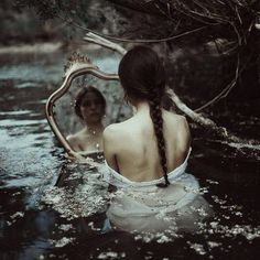 a woman is sitting in the water looking at her reflection with a mirror behind her