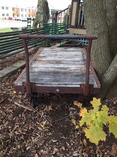 an old wooden bed sitting under a tree in front of a park bench with leaves on the ground