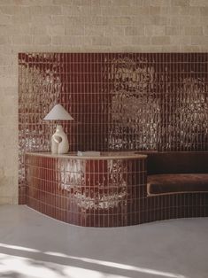 a room with a couch, table and lamp in front of a wall made out of tiles