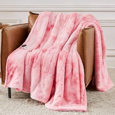 a couch covered in a pink blanket on top of a white rug next to a brown chair