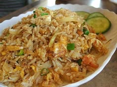 a white bowl filled with rice and vegetables next to cucumbers on a table