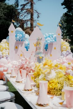 a table topped with lots of balloons and flowers next to a castle shaped cake on top of a white table